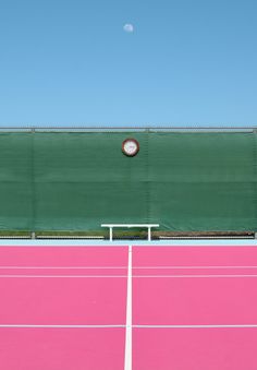 a pink and green tennis court with a ball in the air above it on a clear day