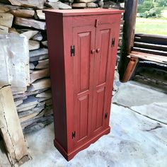 a tall red cabinet sitting next to a pile of firewood in front of a wooden bench