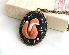 a necklace with an orange fox on it sitting next to a white and pink book