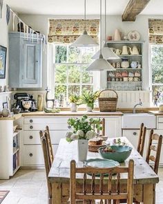 a kitchen filled with lots of wooden furniture and white walls, along with open windows