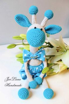 a crocheted giraffe with a blue bow tie sitting next to flowers