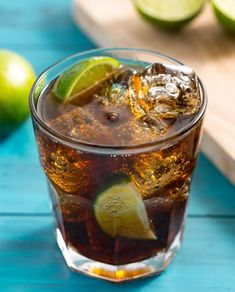 a close up of a drink in a glass with ice and limes on the side