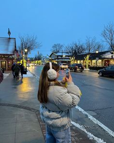 a woman standing on the side of a road holding a cell phone