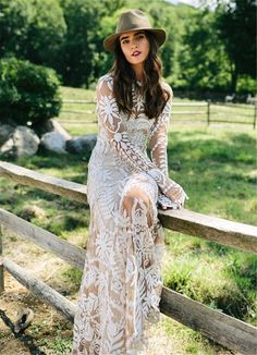 a woman in a dress and hat leaning on a fence