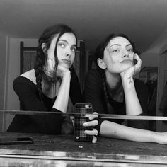 two women sitting at a table with their hands on their chins and one holding a cell phone