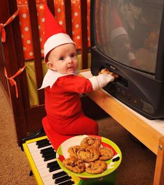 a baby dressed in elf clothes is playing with cookies on the piano while wearing an elf's hat