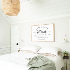 a bed with white sheets and pillows in a bedroom next to a wall hanging above it