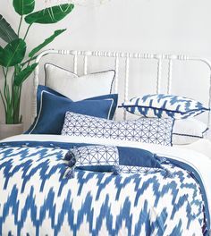 a bed with blue and white pillows on top of it next to a potted plant