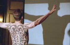 a man with tattoos on his back standing in front of a projection screen holding his arms up