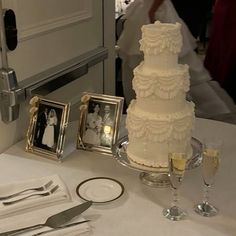 a white wedding cake sitting on top of a table next to silverware and pictures