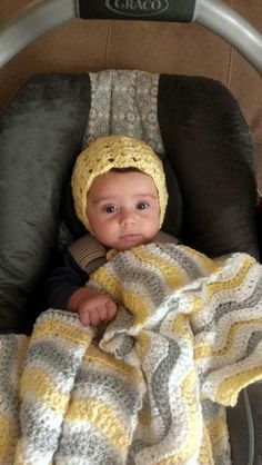 a baby in a car seat with a yellow and gray blanket on it's head