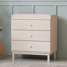 a wooden dresser with three drawers next to a plant and potted plant on the floor