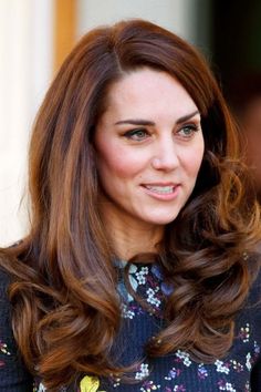 a woman with long brown hair wearing a blue floral dress and smiling at the camera