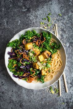 a white bowl filled with noodles and vegetables next to chopsticks on a table