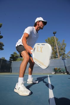 a man holding a tennis racquet on top of a tennis court with trees in the background