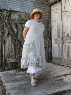 a woman wearing a hat and dress standing on the sidewalk in front of an old building