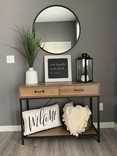 a wooden table topped with a mirror next to a vase filled with flowers and a pillow