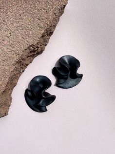 two black earrings sitting next to each other on top of a white surface with a rock in the background