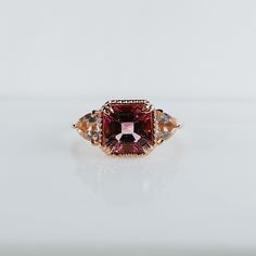 a fancy ring with an orange and pink stone surrounded by multicolored diamonds on a white surface