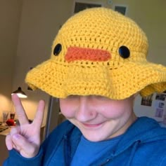 a young boy wearing a crocheted duck hat making the peace sign with his fingers