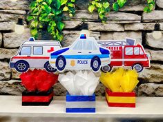 paper cutouts of police cars and firetrucks are displayed in front of a stone wall