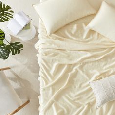 a bed with white sheets and pillows next to a potted plant on the floor