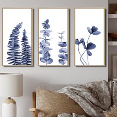 three blue flowers are hanging on the wall next to a lamp and a couch in a living room