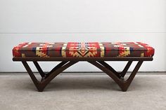 a wooden bench with a colorful blanket on it's backrest in front of a white wall