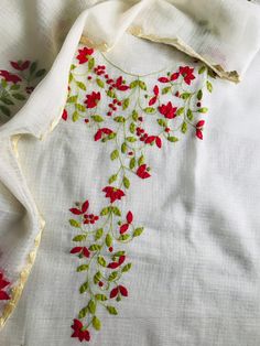 an embroidered white cloth with red flowers on it and green leaves around the edges,