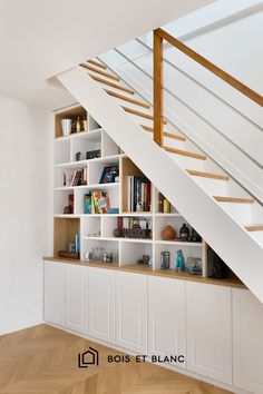 a book shelf under a stair case in a room with white walls and wooden floors