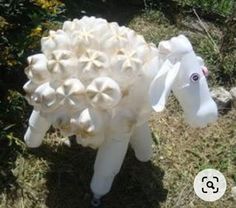 an inflatable sheep is standing on the ground near some bushes and flowers,