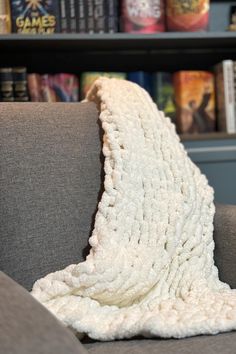 a white blanket sitting on top of a gray chair in front of a book shelf