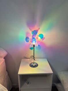 a small white table with a colorful lamp on top of it next to a bed