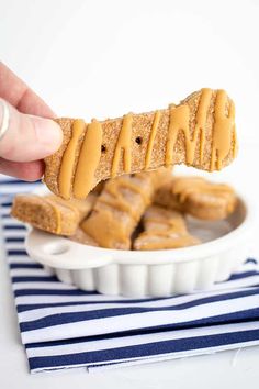 a hand holding a peanut butter pretzel over a white bowl filled with more pretzels