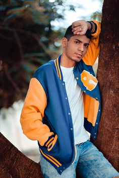 a young man leaning against a tree wearing a blue and yellow jacket