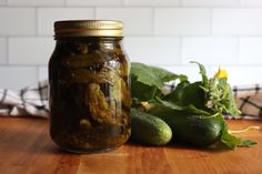 a jar filled with pickles sitting on top of a wooden table next to cucumbers