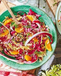 a green bowl filled with salad next to another bowl full of fruit and veggies