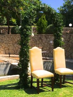 two yellow chairs sitting in the grass next to each other near a pool and stone wall