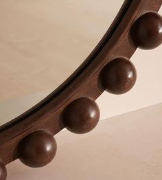 a wooden mirror with balls on the top and bottom edge, sitting on a beige surface