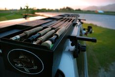 fishing rods are lined up on the back of a truck in front of a body of water