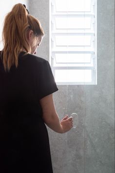 a woman standing in front of a window looking at the shower head and hand held soap dispenser