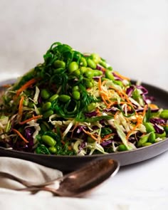 a salad with peas, carrots and sprouts in a black bowl on a white table