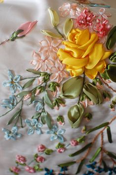 some flowers and leaves are on a white table cloth with blue, pink, yellow, and green stems