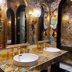 two sinks and mirrors in a bathroom with gold mosaic tiles on the walls, along with chandeliers