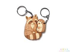 two wooden key chains with an image of a raccoon holding another raccoon