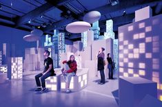 three people are sitting on cubes in a room with blue lights and white walls