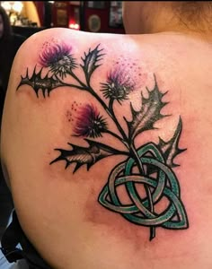 a woman with a tattoo on her back has thistles and leaves in the shape of a celtic knot