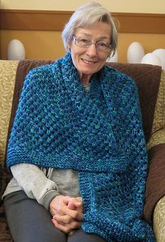 an older woman sitting on a couch wearing a blue knitted shawl and smiling