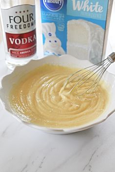 a white bowl filled with batter and whisk next to two bottles of flour