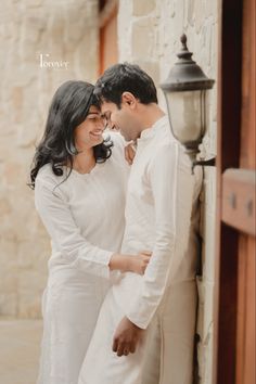 a man and woman standing next to each other in front of a light post holding hands